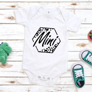 K&ouml;nnte beinhalten: Wei&szlig;er Baby-Strampler mit einem schwarzen Sechseck-Design mit Leopardenmuster und dem Wort "Mini" in schwarzer Schrift.