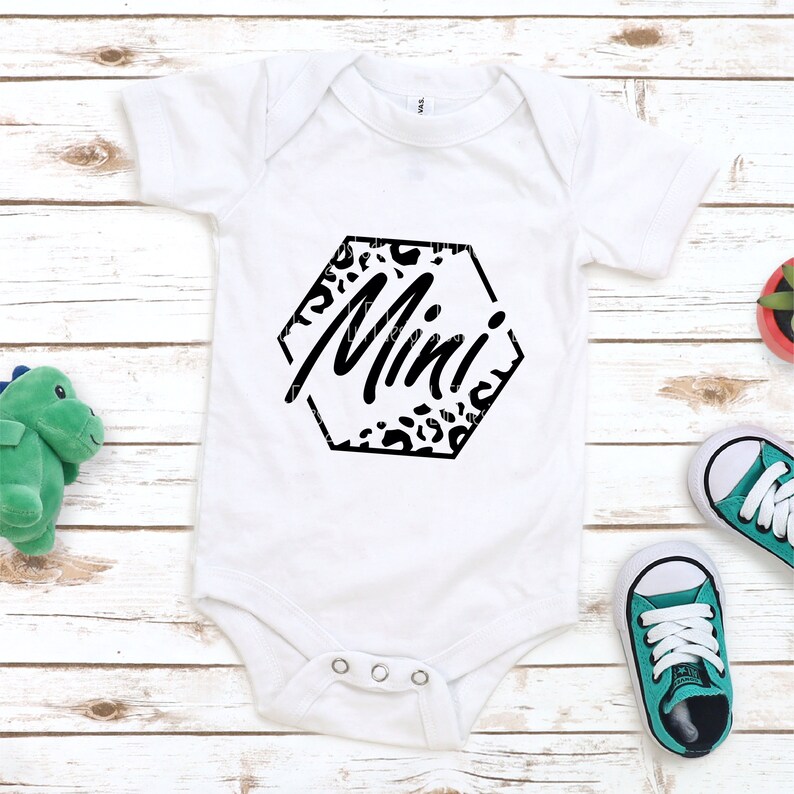 K&ouml;nnte beinhalten: Wei&szlig;er Baby-Strampler mit einem schwarzen Sechseck-Design mit Leopardenmuster und dem Wort "Mini" in schwarzer Schrift.