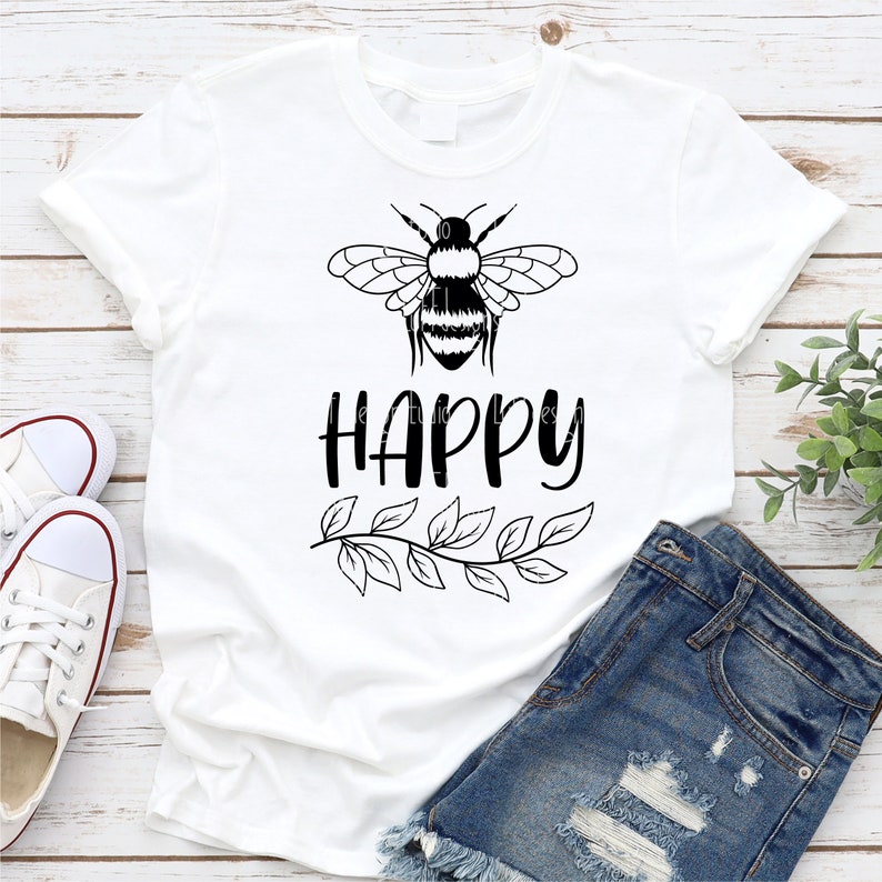May include: White t-shirt with a black bee graphic and the word "HAPPY" printed below the bee. A leafy branch design is below the word "HAPPY".