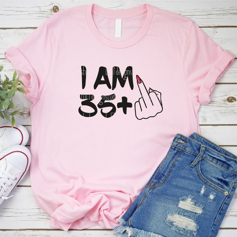 May include: Pink t-shirt with black text that says "I am 35+" with a middle finger emoji.