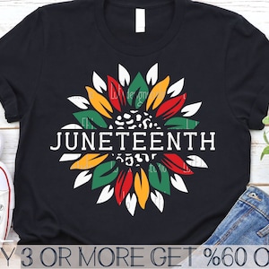 以下が含まれることがあります： 中央に白いひまわりのデザインと「JUNETEENTH」の文字が書かれた黒いTシャツ。