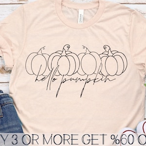 Pode incluir: Uma camiseta rosa claro com um contorno preto de quatro ab&oacute;boras e o texto "hello pumpkin" em uma fonte manuscrita.