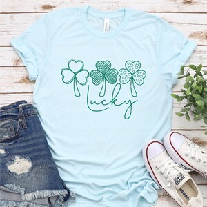 May include: A light blue t-shirt with a green shamrock design and the word "lucky" written in cursive.