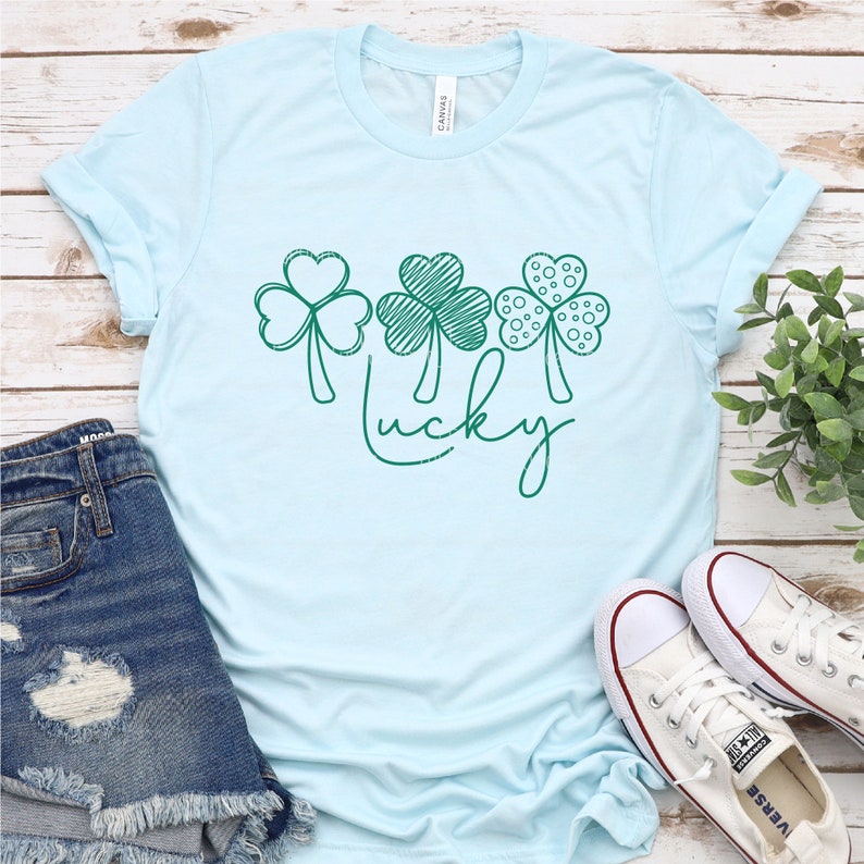 May include: A light blue t-shirt with a green shamrock design and the word "lucky" written in cursive.