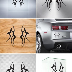 May include: Two black tribal-style decals, each with a unique design, are shown on different surfaces, including a glass display case, a car, and a wooden surface. The decals are symmetrical and feature sharp, angular lines.