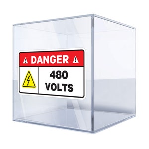Könnte beinhalten: Ein rotes und weißes Warnschild mit einem gelben Blitzsymbol in einem Dreieck. Das Schild lautet "GEFAHR 480 VOLT". Das Schild befindet sich in einem durchsichtigen Glaswürfel.