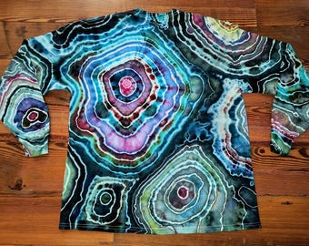 May include: A long-sleeve shirt featuring a vibrant tie-dye pattern that mimics the concentric rings of a geode. The design incorporates shades of deep blue, teal, purple, and magenta, with dark black outlines separating the circular shapes.