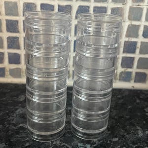 Op de afbeelding: Twee transparante, stapelbare kunststof containers met meerdere compartimenten. De containers zijn leeg en hebben een cilindrische vorm.