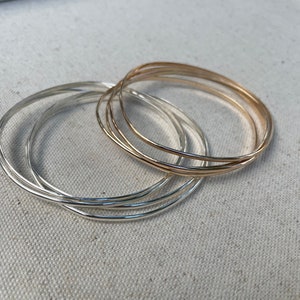 May include: A set of five silver and gold bangles. The bangles are stacked on top of each other, with the gold bangles on top. The bangles are all smooth and shiny.
