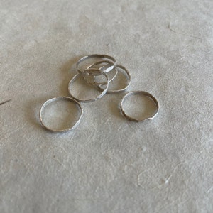 May include: A set of six silver rings with a hammered texture. The rings are stacked on top of each other.