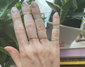 May include: A hand wearing multiple thin gold and silver rings on different fingers.