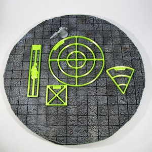 May include: A green plastic set of tabletop gaming templates for role-playing games. The set includes a circle with concentric rings, a square with an X inside, a rectangle, and a triangle with three concentric arcs.