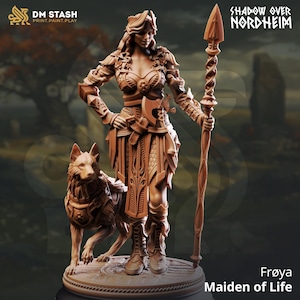 Puede incluir: Una figura marrón de Frøya, la Doncella de la Vida, de la colección Shadow Over Nordheim. La figura es una mujer guerrera con un lobo como compañero, sosteniendo una lanza. La figura tiene una armadura y detalles intrincados, con el logo de DM Stash.
