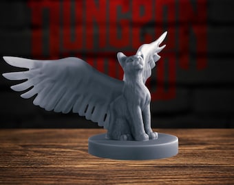 Könnte beinhalten: Eine graue, unbemalte Miniaturfigur einer sitzenden Katze mit großen, gefiederten Flügeln, die zur Seite ausgestreckt sind. Die Katze steht auf einem runden Sockel und blickt mit geneigtem Kopf nach oben. Die Figur besteht aus mattem Material.