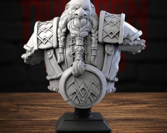 May include: A grey resin bust of a bearded dwarf warrior featuring intricate braided hair, detailed shoulder armour with geometric patterns, and a circular chest emblem with a mountain-like symbol, mounted on a black square base.