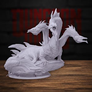 Puede incluir: Una miniatura de resina de color gris claro sin pintar de una criatura dragón de tres cabezas. La figura presenta una cabeza central con la boca abierta, dos cabezas laterales, un cuerpo escamoso y grandes aletas o alas sobre una base rocosa.