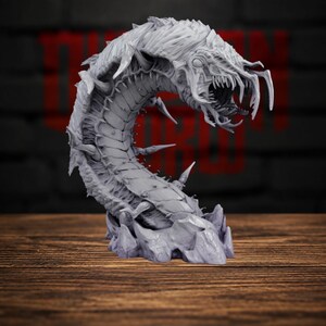 May include: A grey, unpainted resin miniature of a segmented, multi-legged creature with a curved body, sharp spikes along its back, and a wide, open mouth filled with jagged teeth, emerging from a rocky, craggy base structure.