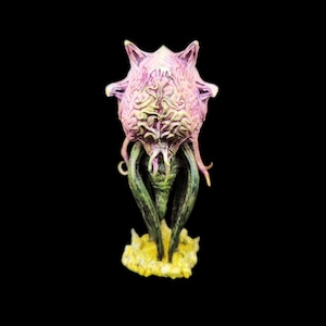Peut inclure: Une créature extraterrestre rose et verte avec des tentacules et une tête bulbeuse, debout sur une base jaune. La créature est une miniature imprimée en 3D.