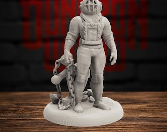 May include: A light gray miniature figurine of a deep-sea diver wearing a vintage-style helmet with a protective cage over the faceplate. The figure stands on a circular base, holding a large metal anchor attached to a heavy chain in one hand.