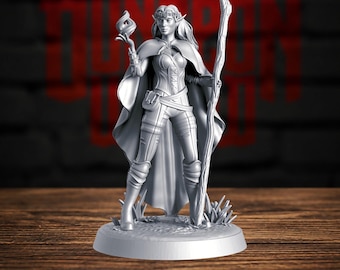 May include: A gray miniature figurine of an elf character wearing a cloak, a floral headband, and fitted armor. The figure holds a staff in one hand and a small flame in the other, standing on a circular base with textured ground details.