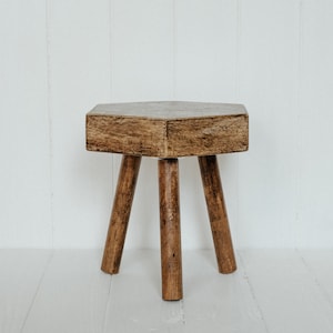 May include: A rustic wooden stool with a hexagonal top and three legs. The stool is made of dark brown wood and has a distressed finish.