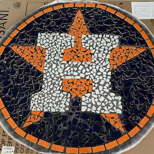 May include: Circular mosaic table top with the Houston Astros logo. The design features a large orange star and the letter "H" in white and orange, set against a dark blue background. The border is orange.