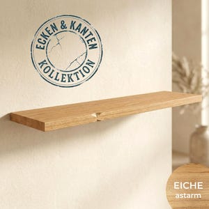 Op de afbeelding: Een zwevend plankje van natuurlijk eikenhout, gemonteerd aan een lichtgekleurde muur. Het plankje heeft een rechthoekige vorm met een inkeping en maakt deel uit van de "Ecken & Kanten Kollektion". De houtnerf is zichtbaar.