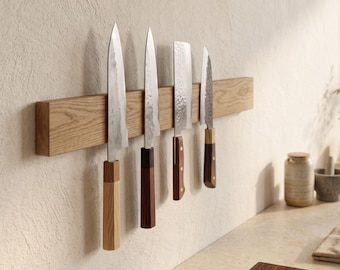 Peut inclure: Une barre magnétique en bois montée horizontalement sur un mur, supportant quatre couteaux de cuisine aux lames variées et aux manches en bois. Les lames sont métalliques, dont une martelée et une autre portant des caractères gravés.