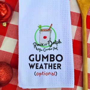 May include: White kitchen towel with a red and green illustration of a pot of gumbo. The text "Roux-Dolph The Gumbo Pot" and "GUMBO WEATHER (optional)" is printed on the towel.
