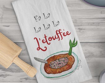 Może przedstawiać: Biały ręcznik kuchenny z napisem "Fa La La La La L'etouffee" w czarnym i czerwonym skrypcie. Ręcznik przedstawia akwarelową ilustrację talerza z jedzeniem i widelcem. Drewniany wałek do ciasta i jabłka są w tle.
