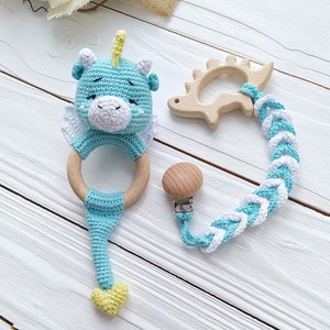 May include: A blue crocheted baby rattle with a wooden ring and a yellow heart. The rattle is attached to a braided cord with a wooden teether and a clip.