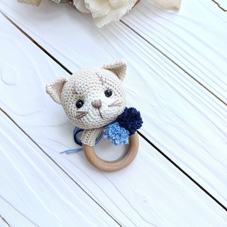 Op de afbeelding: Een gehaakte kattenrammelaar met blauwe pompoenen bevestigd aan een houten ring.