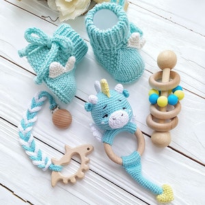May include: A set of baby toys including a pair of blue knitted booties, a blue knitted unicorn rattle, a wooden teether, and a wooden rattle with blue and yellow beads.