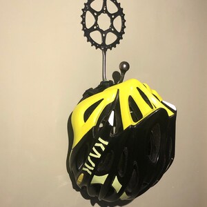 Puede incluir: Un casco de bicicleta negro y amarillo colgado de un gancho de pared hecho de un plato de cadena de bicicleta.