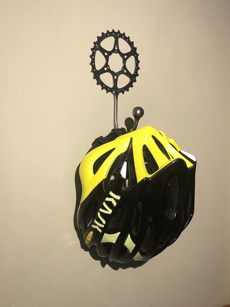 Puede incluir: Un casco de bicicleta negro y amarillo colgado de un gancho de pared hecho de un plato de cadena de bicicleta.