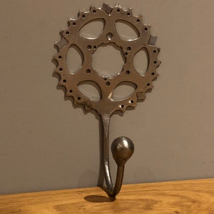 Puede incluir: Un gancho de pared de metal plateado con un dise&ntilde;o de engranaje redondo.