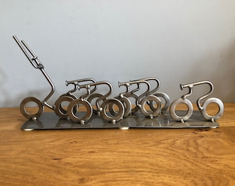 Puede incluir: Una escultura de metal de una bicicleta tirando de un tren de bicicletas más pequeñas. La escultura está hecha de metal soldado y tiene un aspecto rústico e industrial.