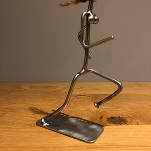 May include: A silver metal sculpture of a person running. The sculpture is made of nuts and bolts and has a copper wire for hair.