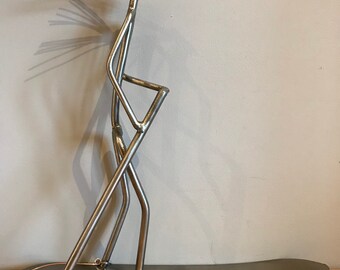 May include: A metal sculpture of a person standing on a surfboard, holding a paddle. The sculpture is made of recycled metal and has a rustic, industrial look.