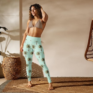 May include: Light blue leggings with a repeating pattern of palm trees. The leggings have a high waist and a fitted design. The palm trees are green with red accents. The leggings are made of a soft, stretchy material.