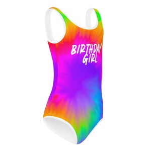 Puede incluir: Un traje de ba&ntilde;o de te&ntilde;ido anudado arco&iacute;ris con tirantes blancos y un ribete blanco. El traje de ba&ntilde;o tiene el texto "Birthday Girl" en blanco.