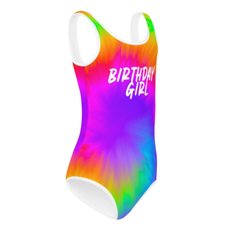 Puede incluir: Un traje de ba&ntilde;o de te&ntilde;ido anudado arco&iacute;ris con tirantes blancos y un ribete blanco. El traje de ba&ntilde;o tiene el texto "Birthday Girl" en blanco.