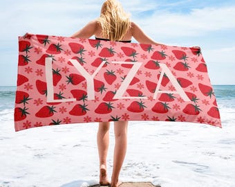 May include: A pink beach towel with a white strawberry pattern and the name "LYZA" printed in white.