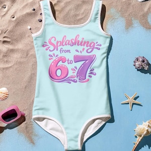 Op de afbeelding: Een lichtblauw badpak met witte rand. Het badpak heeft de tekst "Splashing from 6 to 7" in roze en paars. Het badpak is ontworpen voor kinderen.