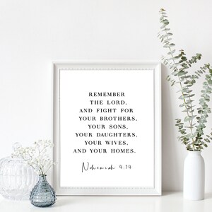 Puede incluir: Una impresi&oacute;n enmarcada en blanco con una cita inspiradora en blanco y negro de la Biblia, "Recuerda al Se&ntilde;or, y lucha por tus hermanos, tus hijos, tus hijas, tus esposas y tus hogares. Nehem&iacute;as 4:14". La impresi&oacute;n est&aacute; sobre una superficie blanca con un jarr&oacute;n de vegetaci&oacute;n y un peque&ntilde;o jarr&oacute;n de vidrio con flores blancas.