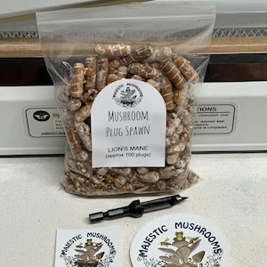May include: A clear plastic bag filled with brown mushroom plugs, labeled "Majestic Mushrooms Mushroom Plug Spawn Lion's Mane (approx 100 plugs)".  The bag is sealed with a heat sealer.  Two stickers are included, both with the Majestic Mushrooms logo, a mushroom with a frog and bees on top.  One sticker is square and the other is round.  A drill bit is included for drilling holes in logs for mushroom cultivation.