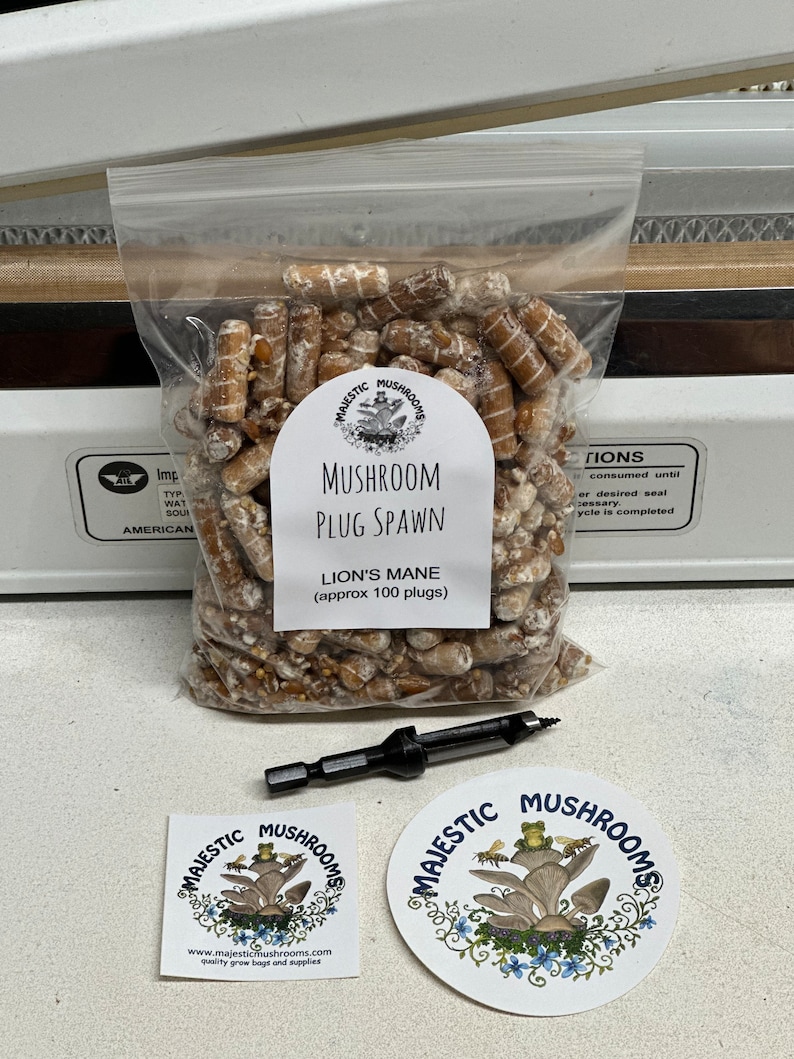 May include: A clear plastic bag filled with brown mushroom plugs, labeled "Majestic Mushrooms Mushroom Plug Spawn Lion's Mane (approx 100 plugs)".  The bag is sealed with a heat sealer.  Two stickers are included, both with the Majestic Mushrooms logo, a mushroom with a frog and bees on top.  One sticker is square and the other is round.  A drill bit is included for drilling holes in logs for mushroom cultivation.