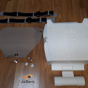May include: A white plastic Star Wars Stormtrooper costume kit with a white fabric cape, two black and gray straps, and a white plastic Imperial symbol.