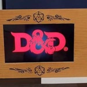 May include: A wooden D&D game screen with a central panel displaying the D&D logo in red. The screen has decorative etched designs and is hinged for folding. The wood has a light brown finish.