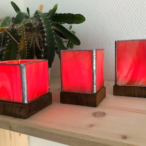 May include: Three red stained glass candle holders with wooden bases. The candle holders are lit and glowing.